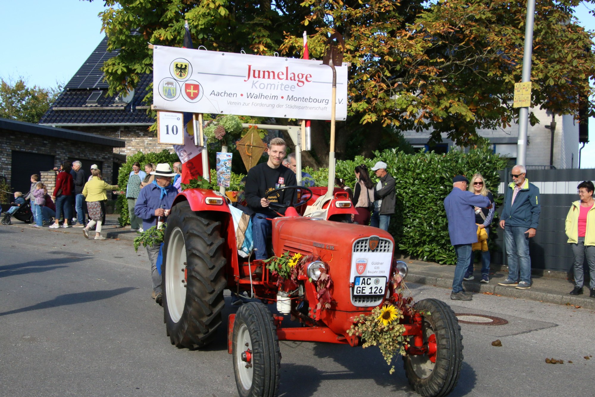 Roter Oldtimertraktor mit Festwagen beim Erntedankzug Walheim 2026.